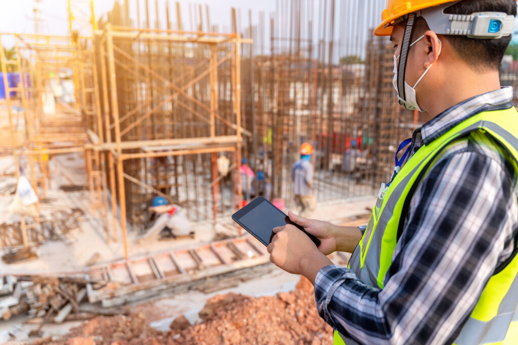 Construction civil engineer or architect with hardhat on construction site checking schedule and building foundations project on tablet computer at construction site
